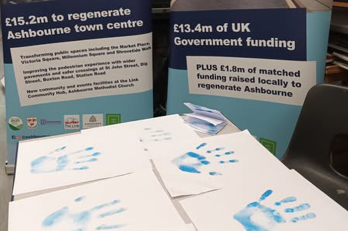 A number of handprints on white paper in blue ink, beside two Ashbourne Reborn banners
