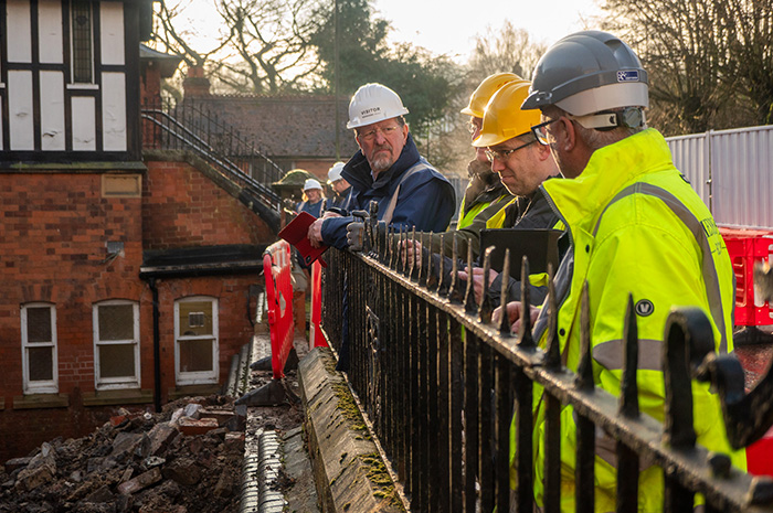 Men in hard hats lean over black railings to examine progress at The Link building site